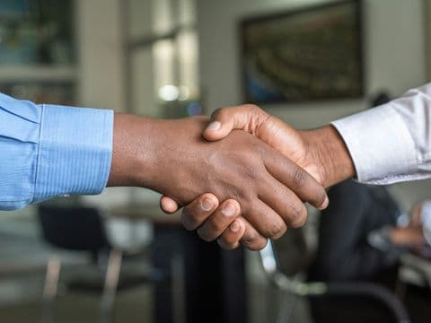 Two parties shaking hands across a table after reaching agreement